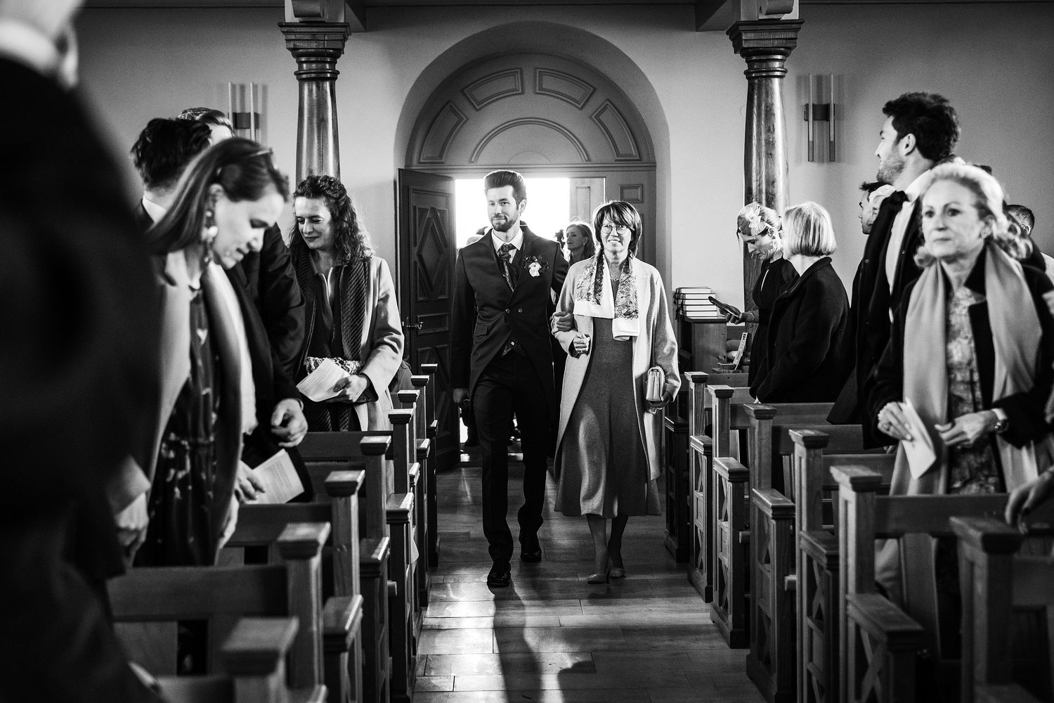 TLOOK photographe de mariage de style documentaire, aux portes des iris cérémonie à l'église le marié entre au bras de sa maman
