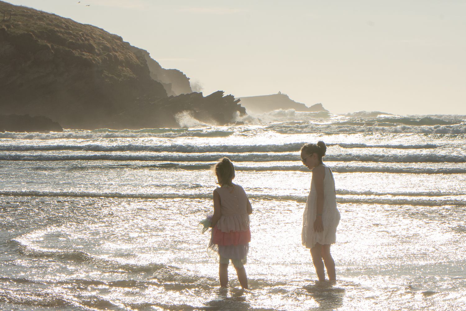 Waves crashing behind children playing on a shore in Cornwall, UK