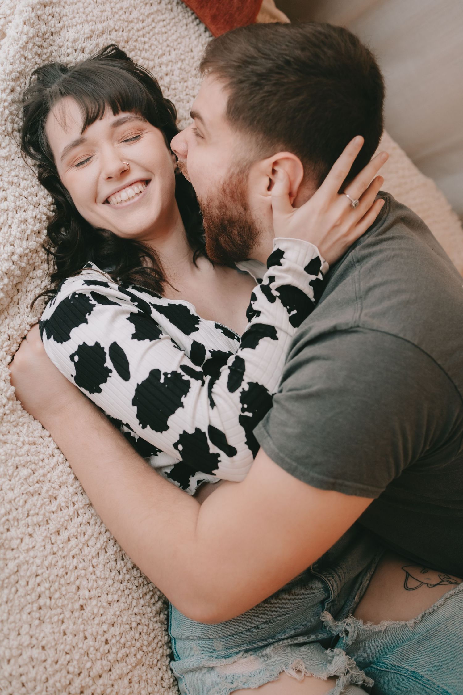 A couple laying in an embrace he is making a funny face she is smiling with her eyes closed.