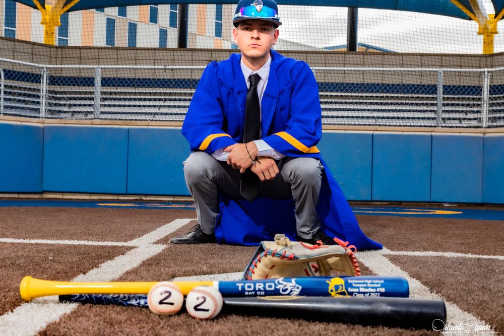 Baseball player in blue uniform sits on field with bats and equipment.