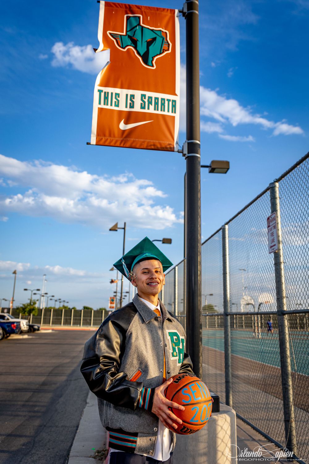 Person holding basketball poses near orange Texas state flag and school banners.