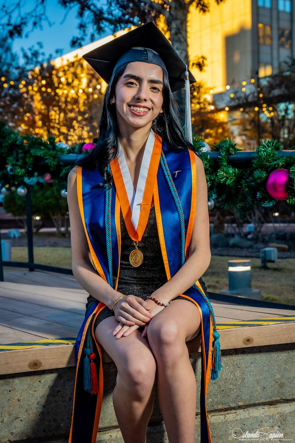 Graduate in academic regalia sits outdoors during golden hour.