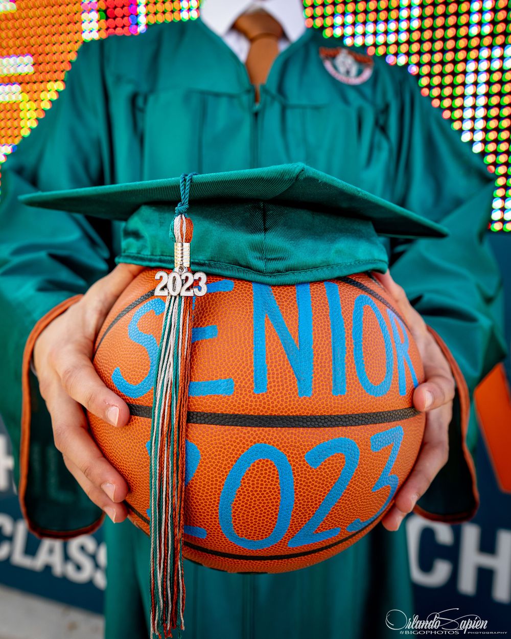 Graduation photo featuring a basketball with class tassel against green graduation gown.