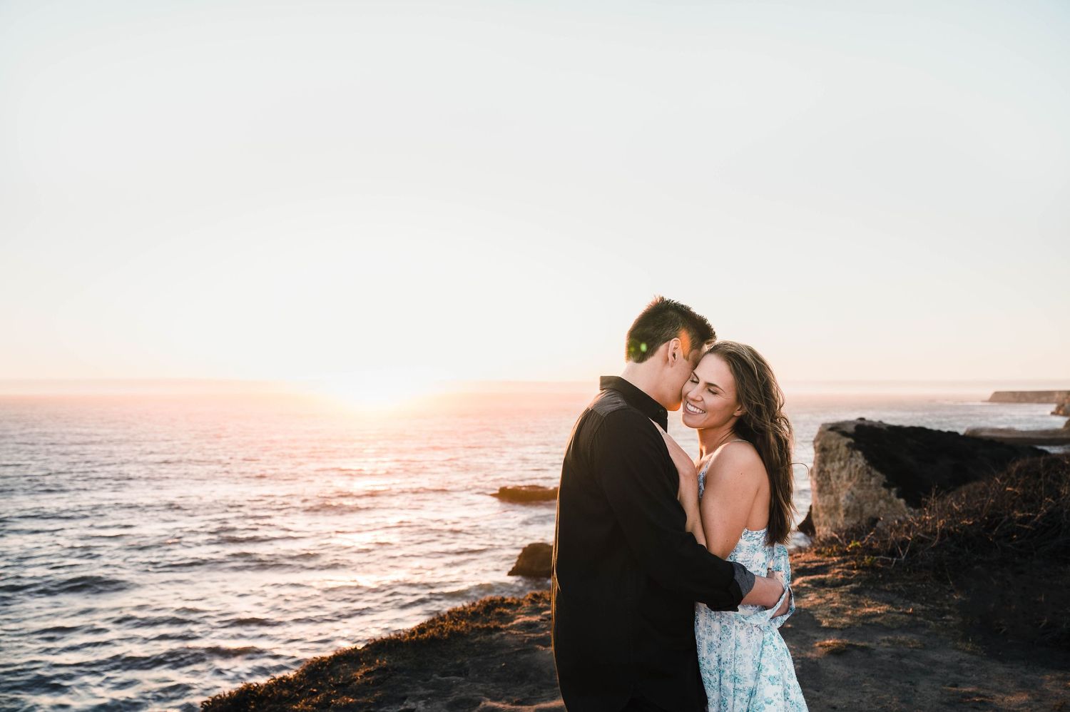 A romantic sunset embrace on the California coast with crashing waves below.