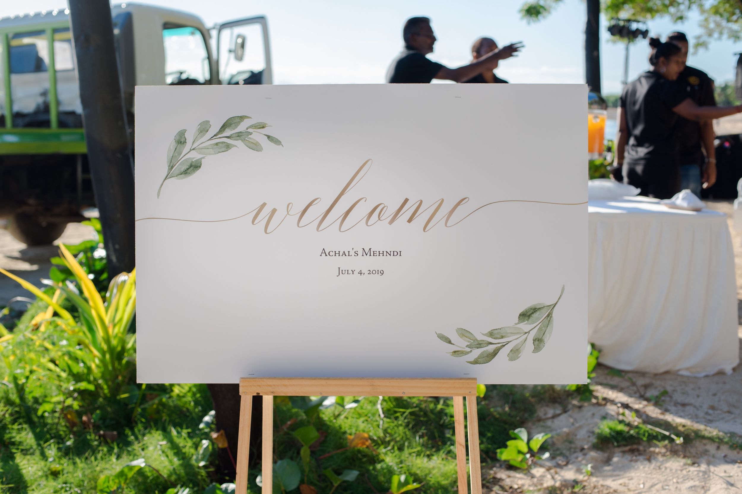 Elegant welcome sign with cursive text and watercolor greenery design at an outdoor event.