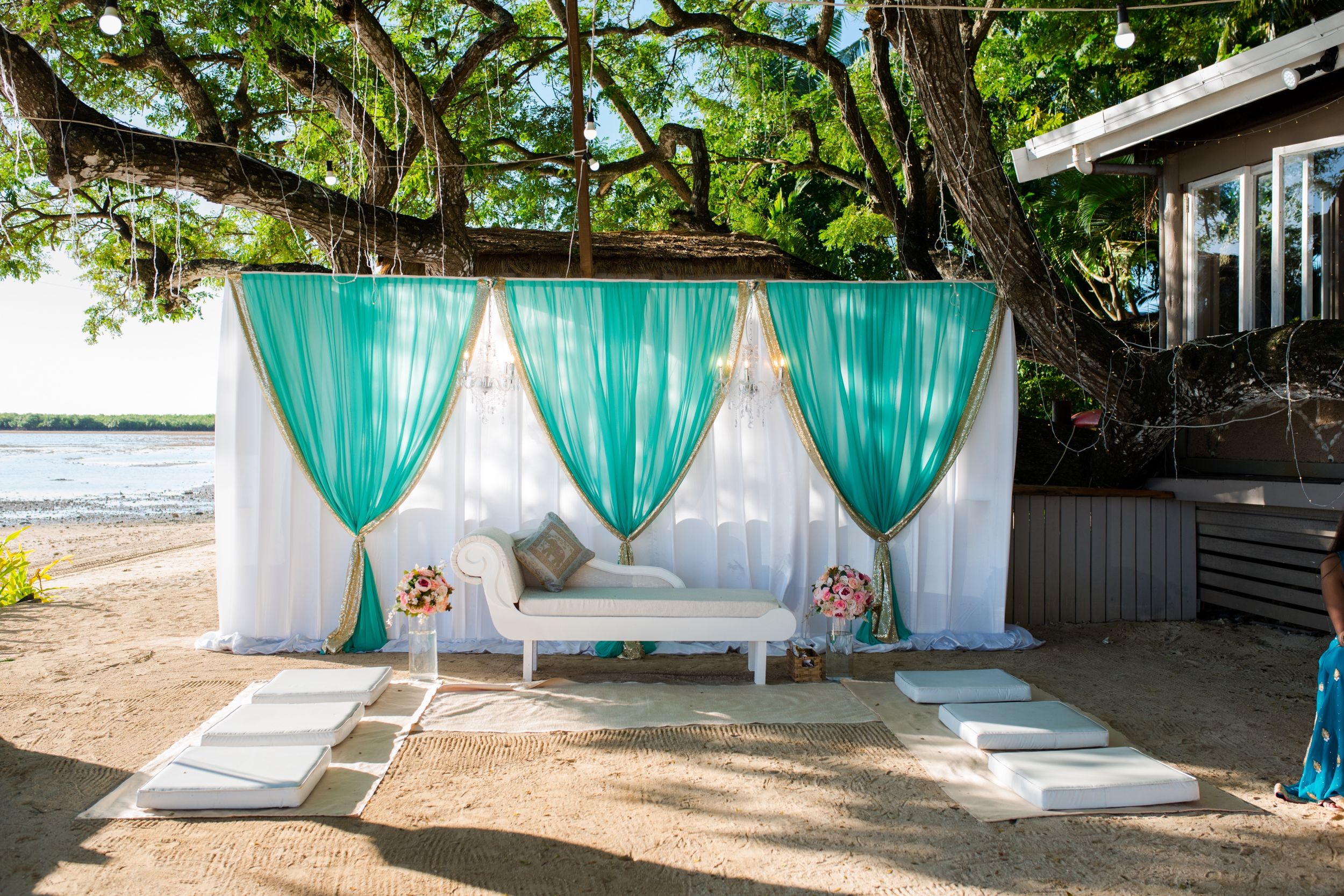Outdoor seating area with turquoise drapes and white furniture against a waterfront backdrop.