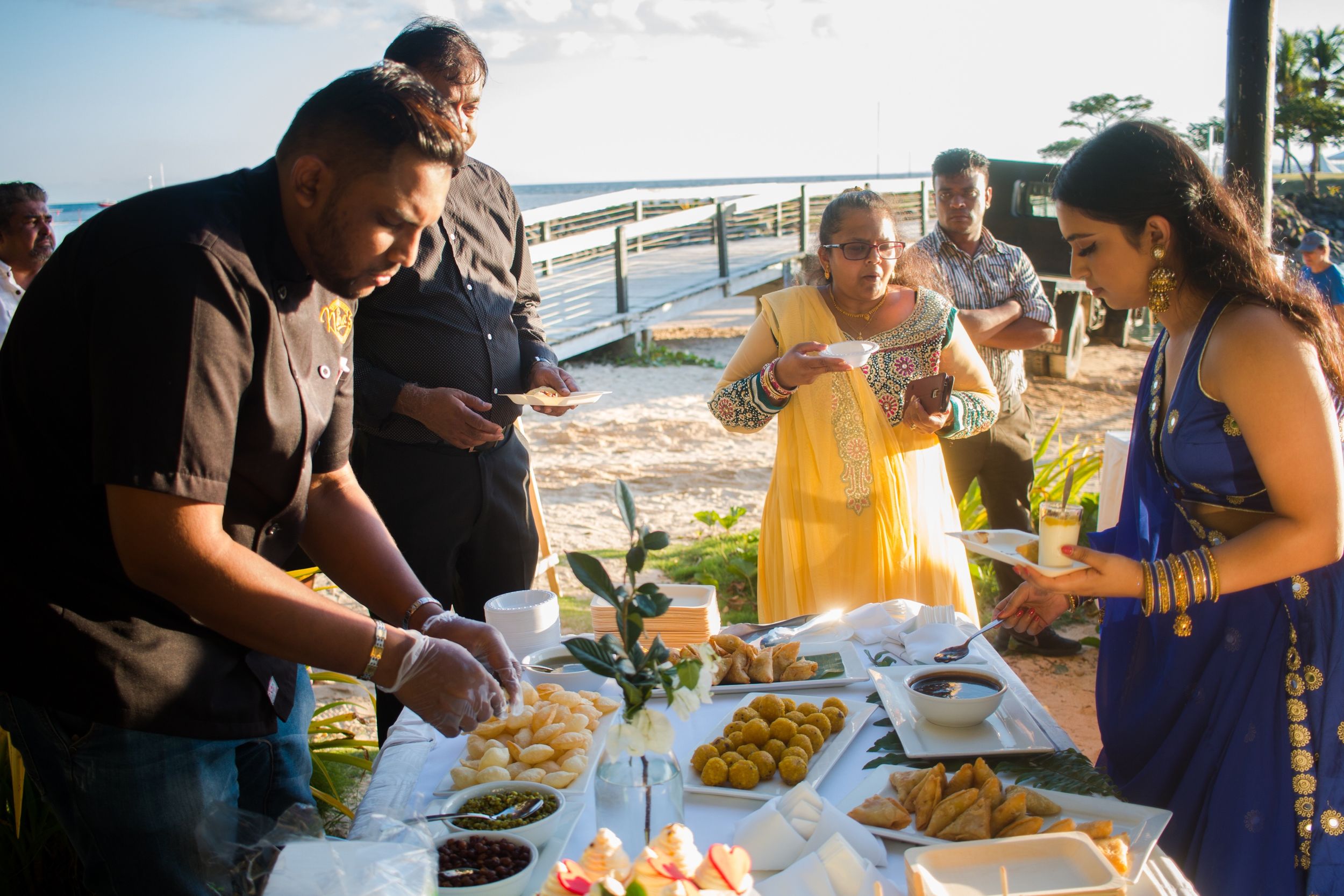 Guests serve themselves from a buffet spread at an outdoor waterfront celebration.