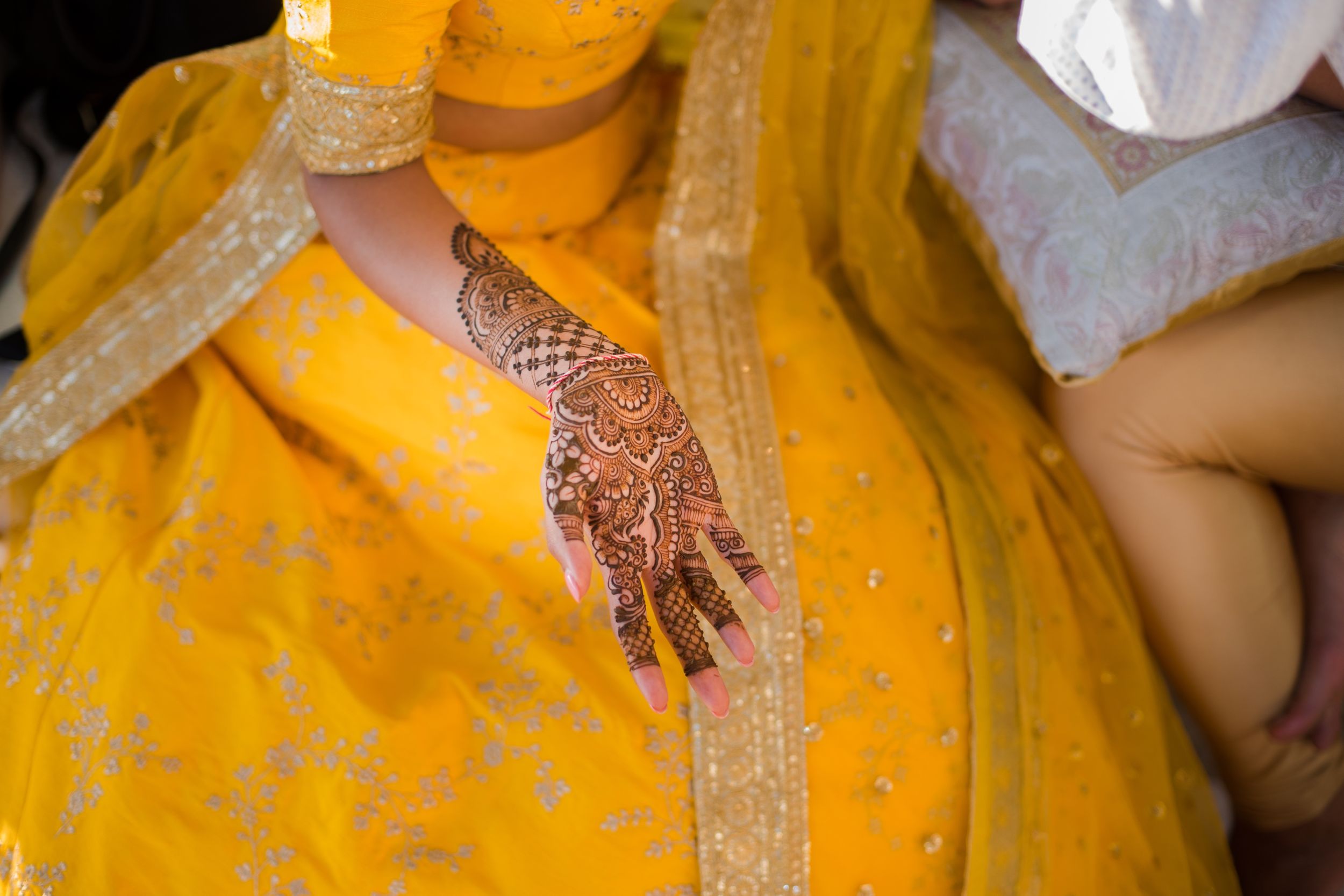 Detailed henna design displayed on hand against yellow fabric with gold embellishments.