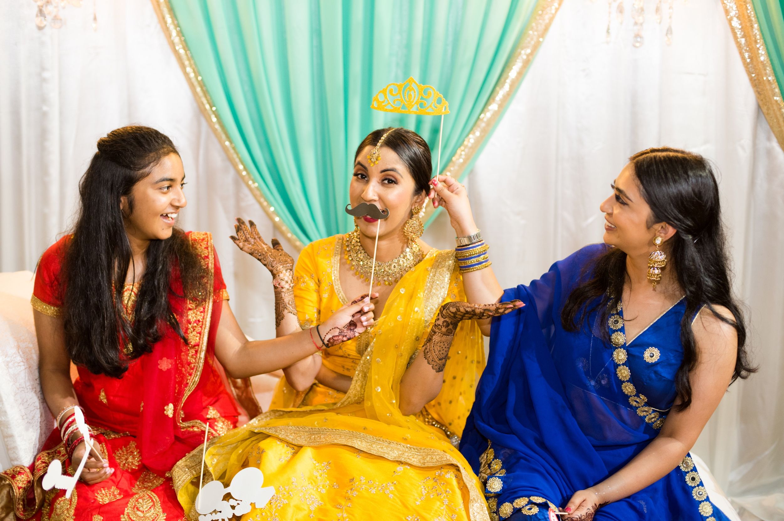 Three friends in vibrant saris share joyful moments at a traditional Indian celebration.