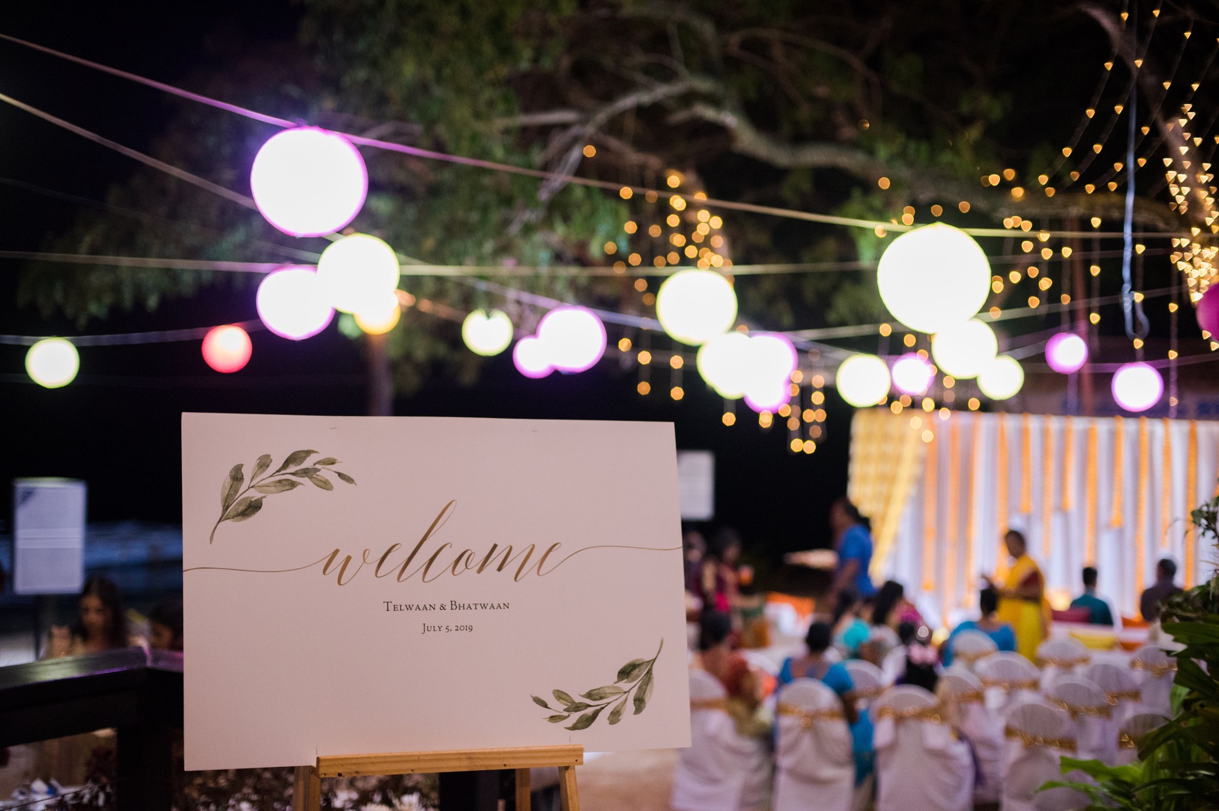 Welcome sign with paper lanterns and string lights at outdoor evening celebration.