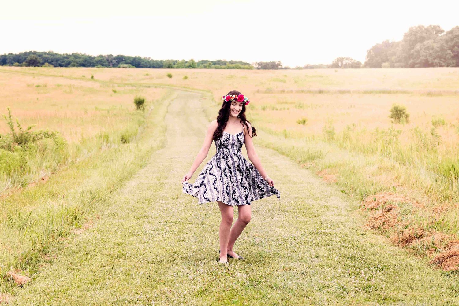 Dancing figure in patterned dress twirling on grass path through golden summer field.