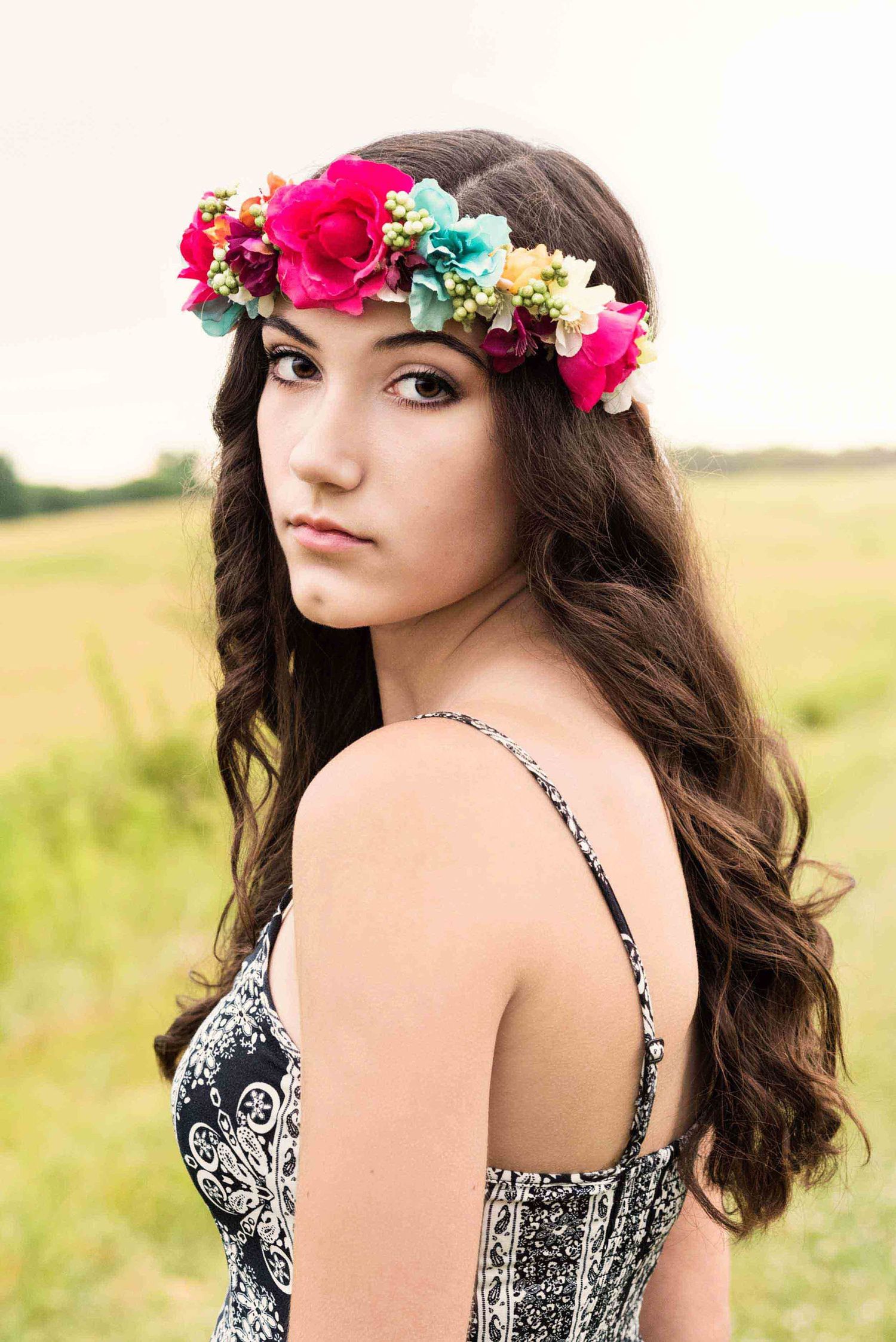 Portrait featuring bright floral crown and patterned dress in summer field setting.