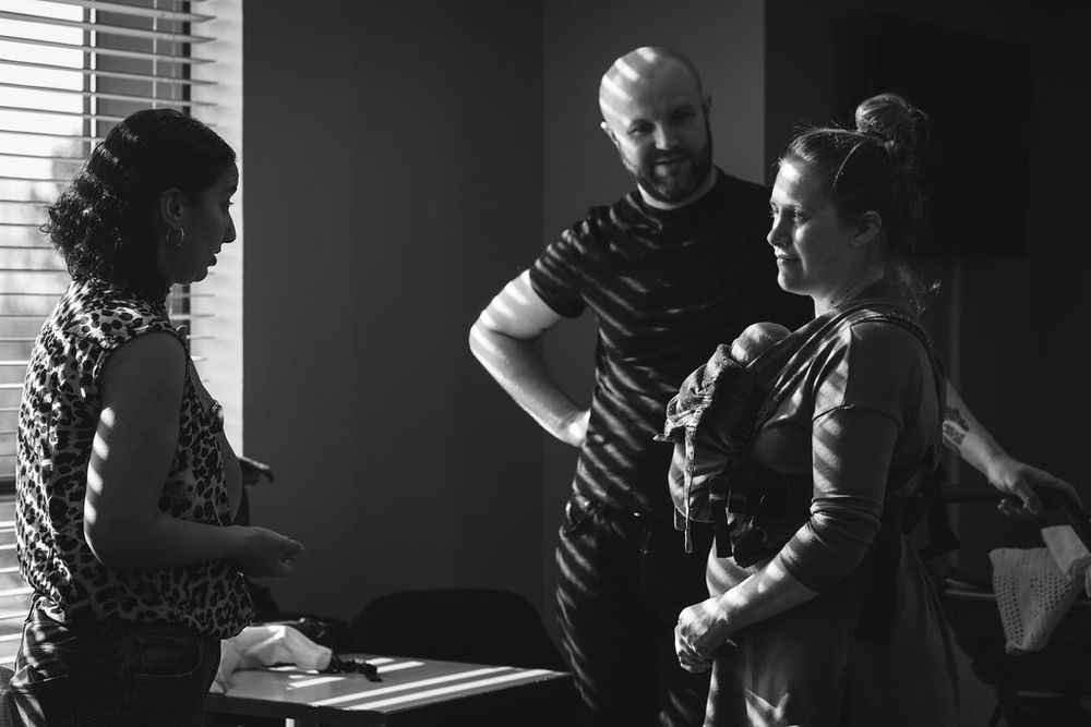 People having an animated conversation in a dimly lit room near a window.