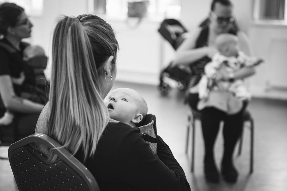 Baby looking upward while being held during indoor gathering.