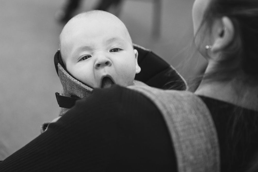 A small infant looks over a caregiver's shoulder in a candid black and white portrait.