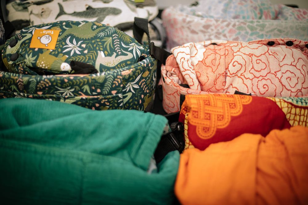 Colorful baby wraps and carriers in various patterns and fabrics are displayed together.