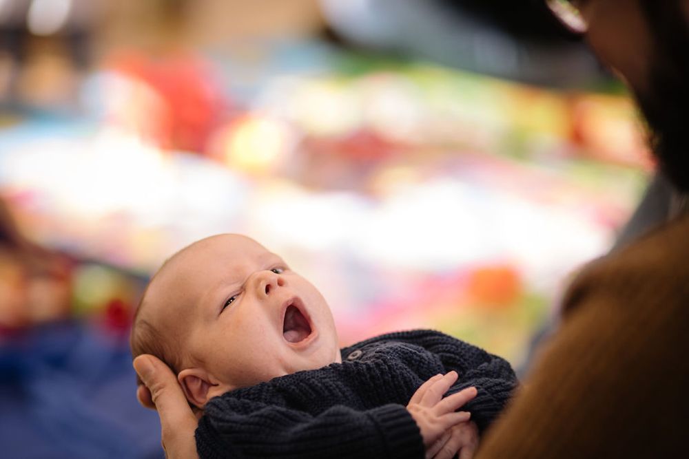 A close-up shot of a yawning baby against a colorful blurred background.