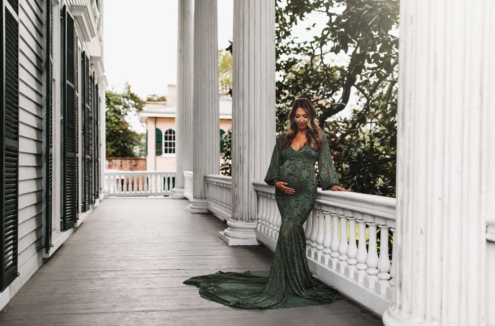 Dramatic emerald dress flows across white plantation porch with classic columns.
