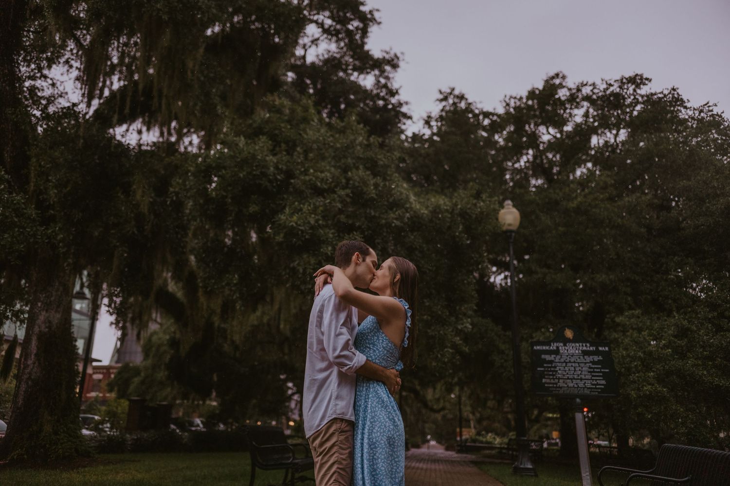 A romantic couple embraces at sunset beneath Spanish moss-draped trees in a park.