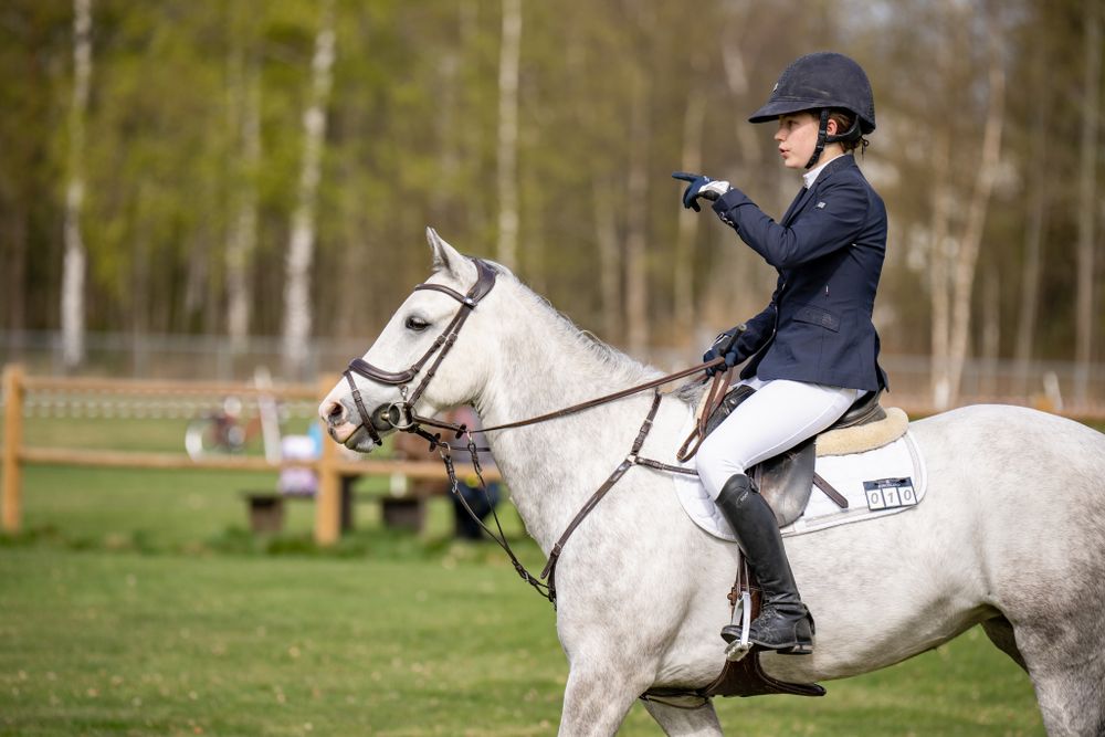 A white horse being ridden in an outdoor equestrian competition.