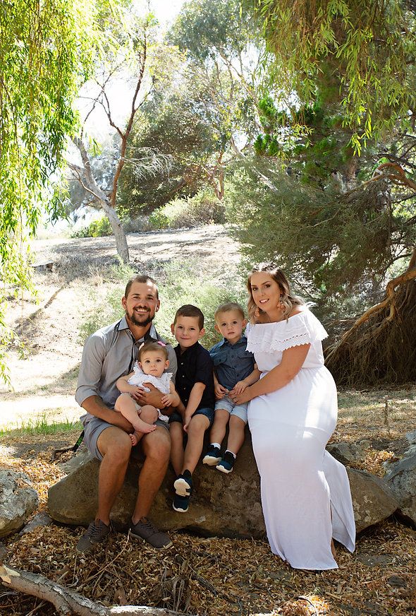 Tayla, her husband and her three children sitting on a log smiling