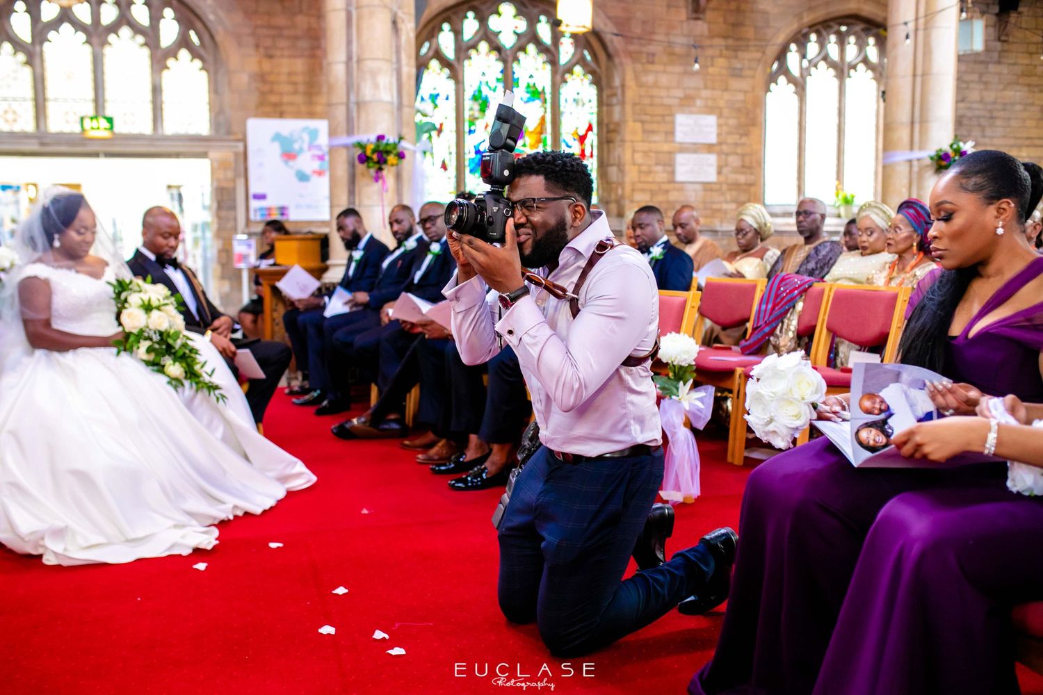 Wedding celebration in a church with guests wearing purple dresses on red carpet.