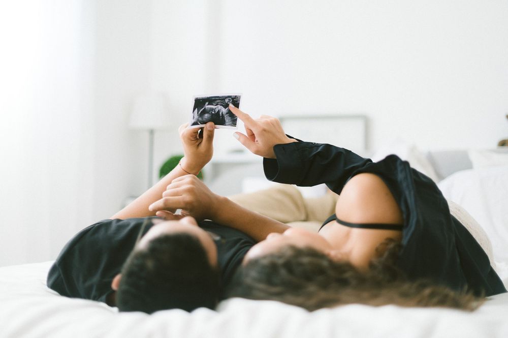 A couple lying on bed looking at ultrasound photos together.