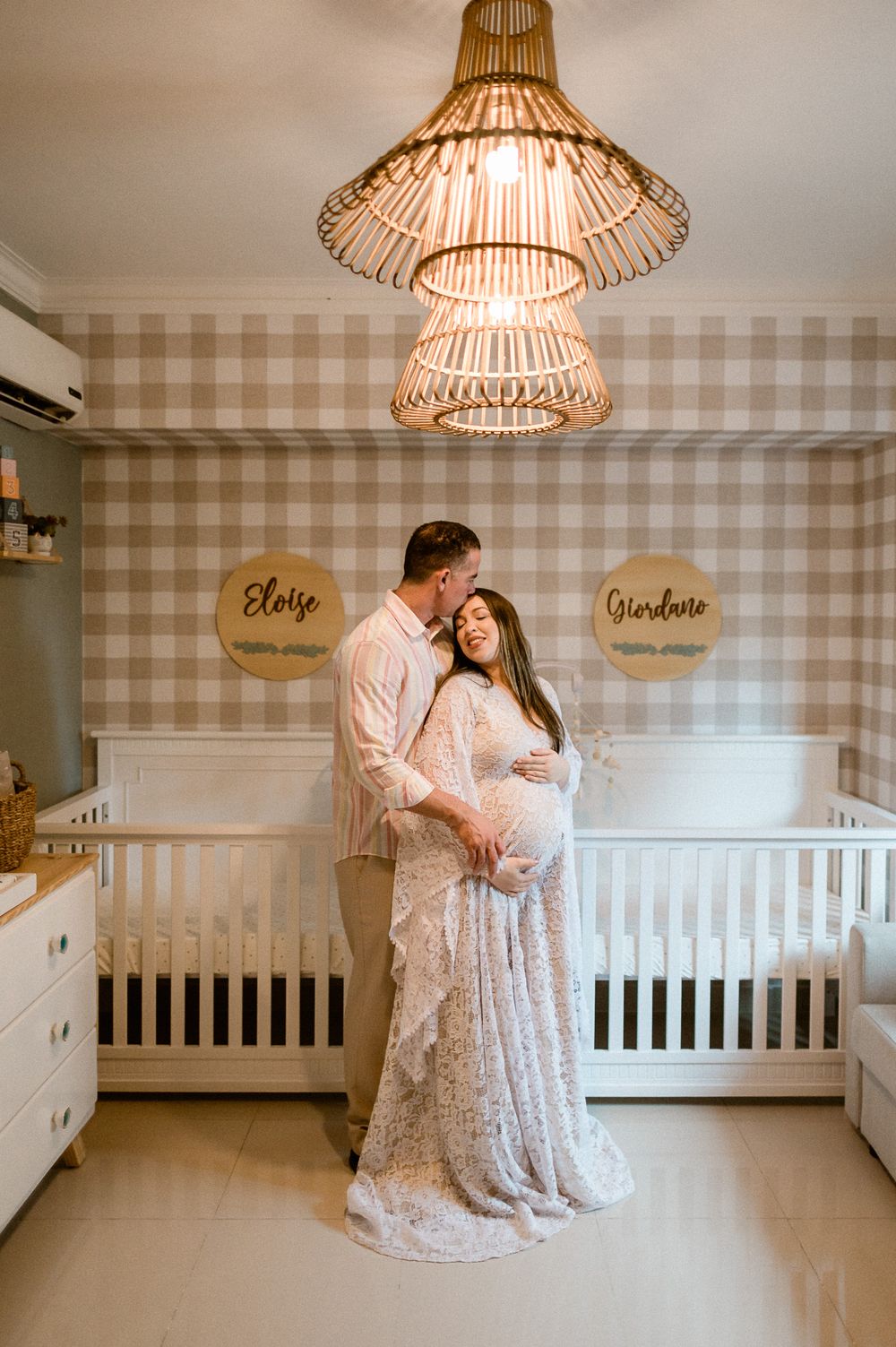 A nursery room with rattan light fixtures and gingham wallpaper features a white crib and dresser.