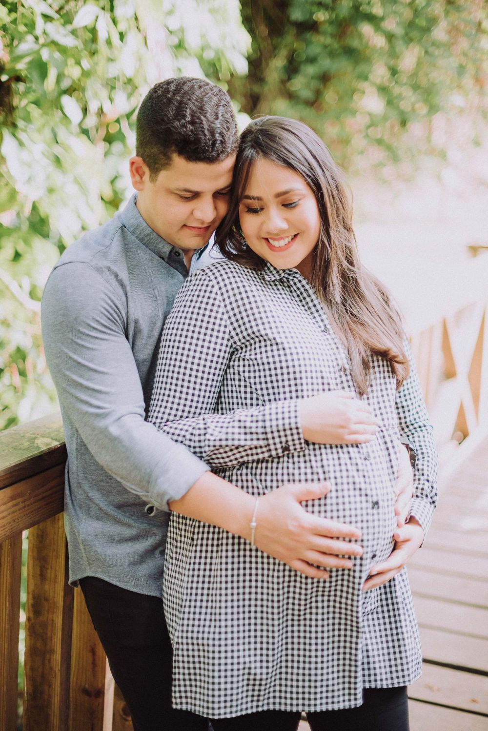 A couple embraces on a wooden deck while wearing coordinating gray and gingham outfits.
