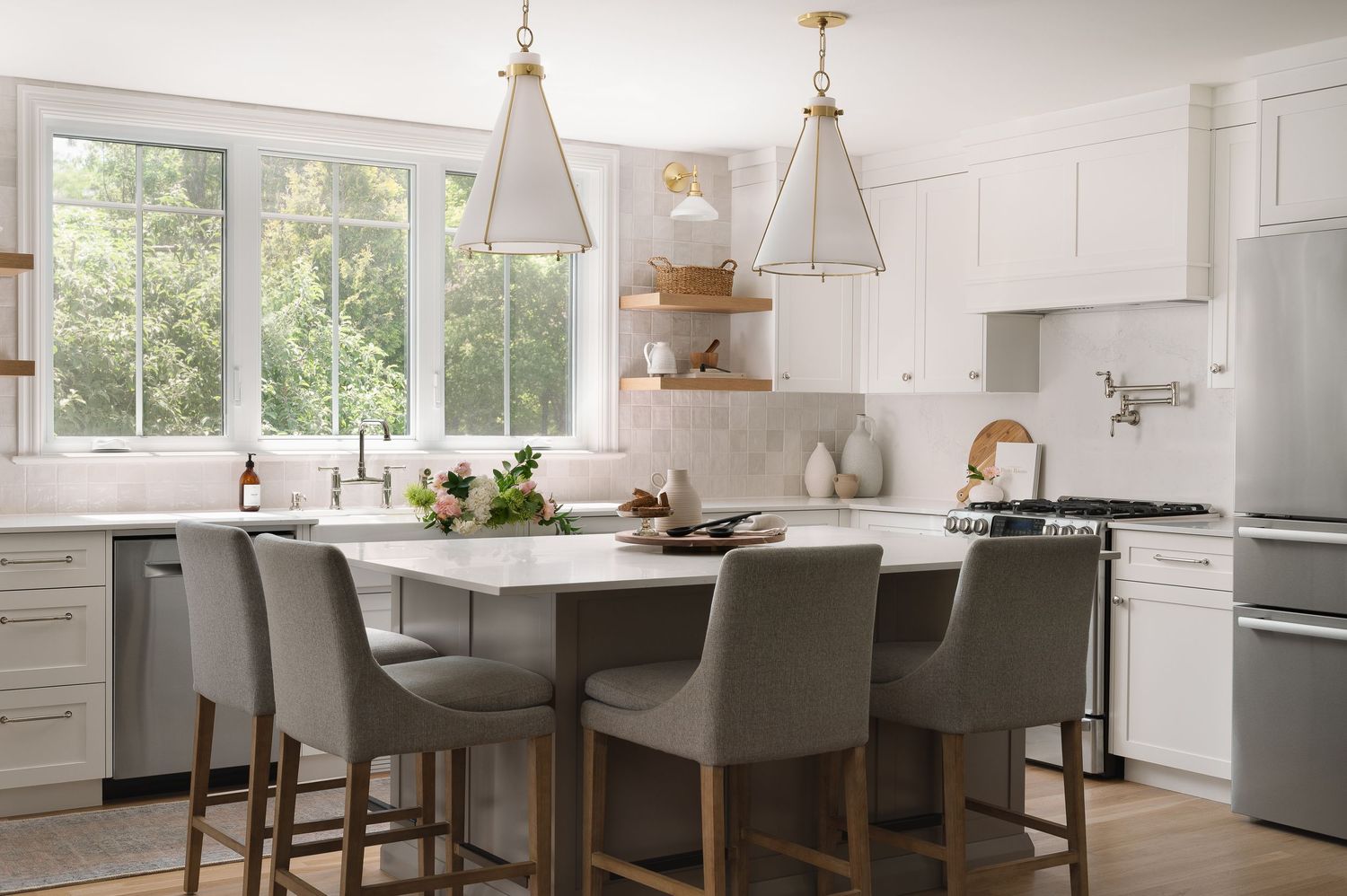 Modern white kitchen with gray island seating, pendant lights, and bright windows.