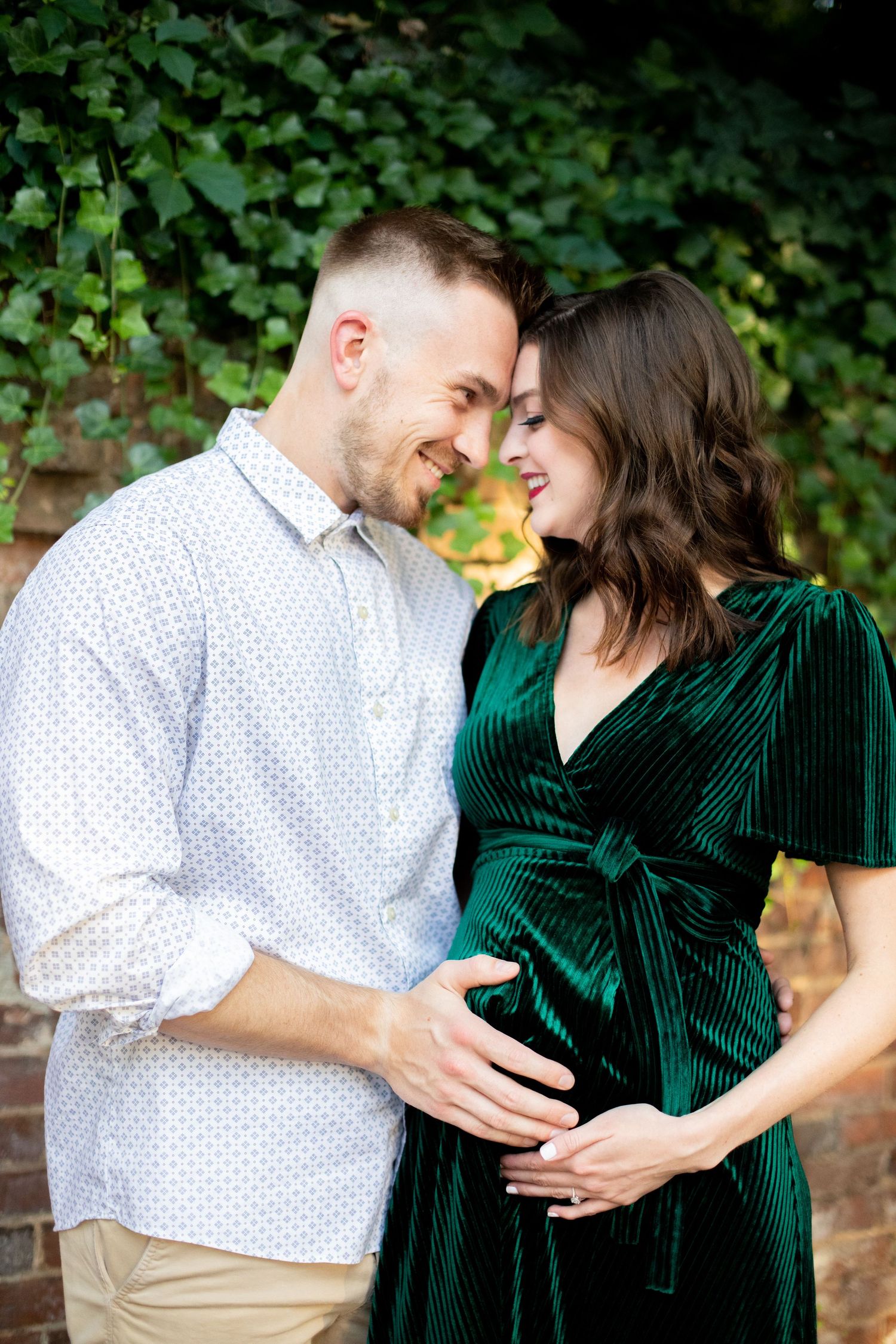 Joyful maternity photos in a garden setting with emerald green dress.