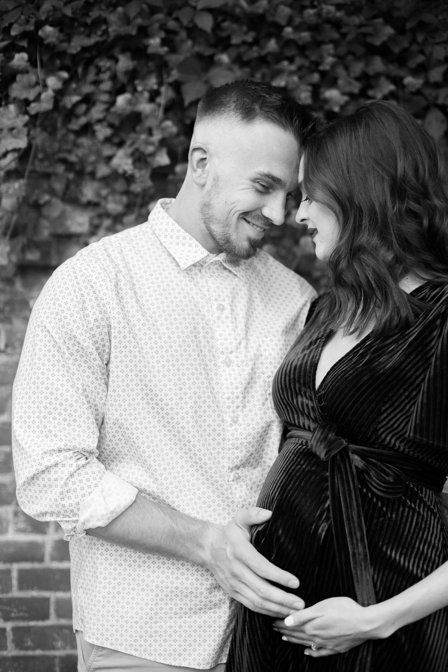 Black and white maternity photos against a leafy background and brick wall.