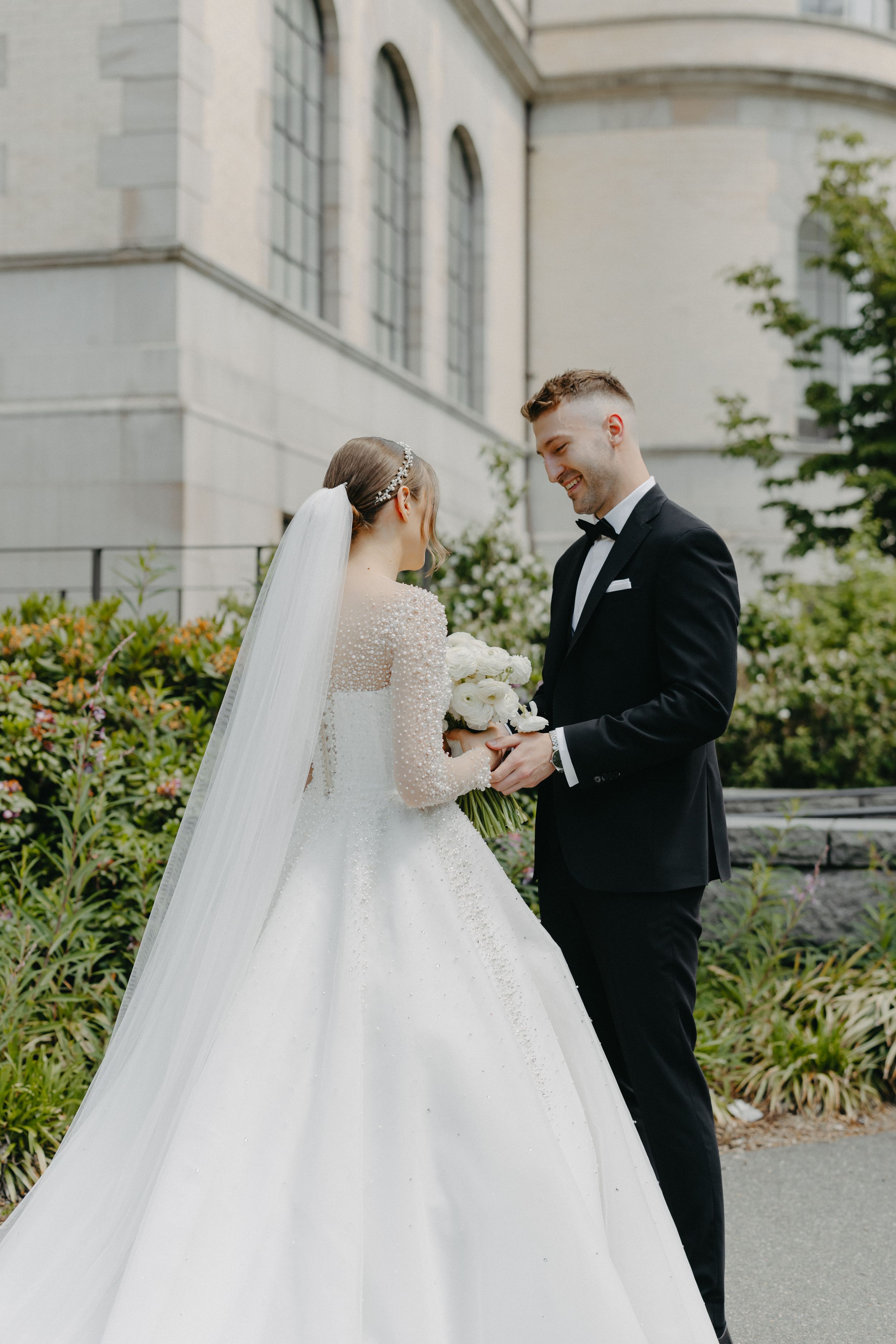 Elegant wedding couple standing together on church grounds surrounded by greenery.