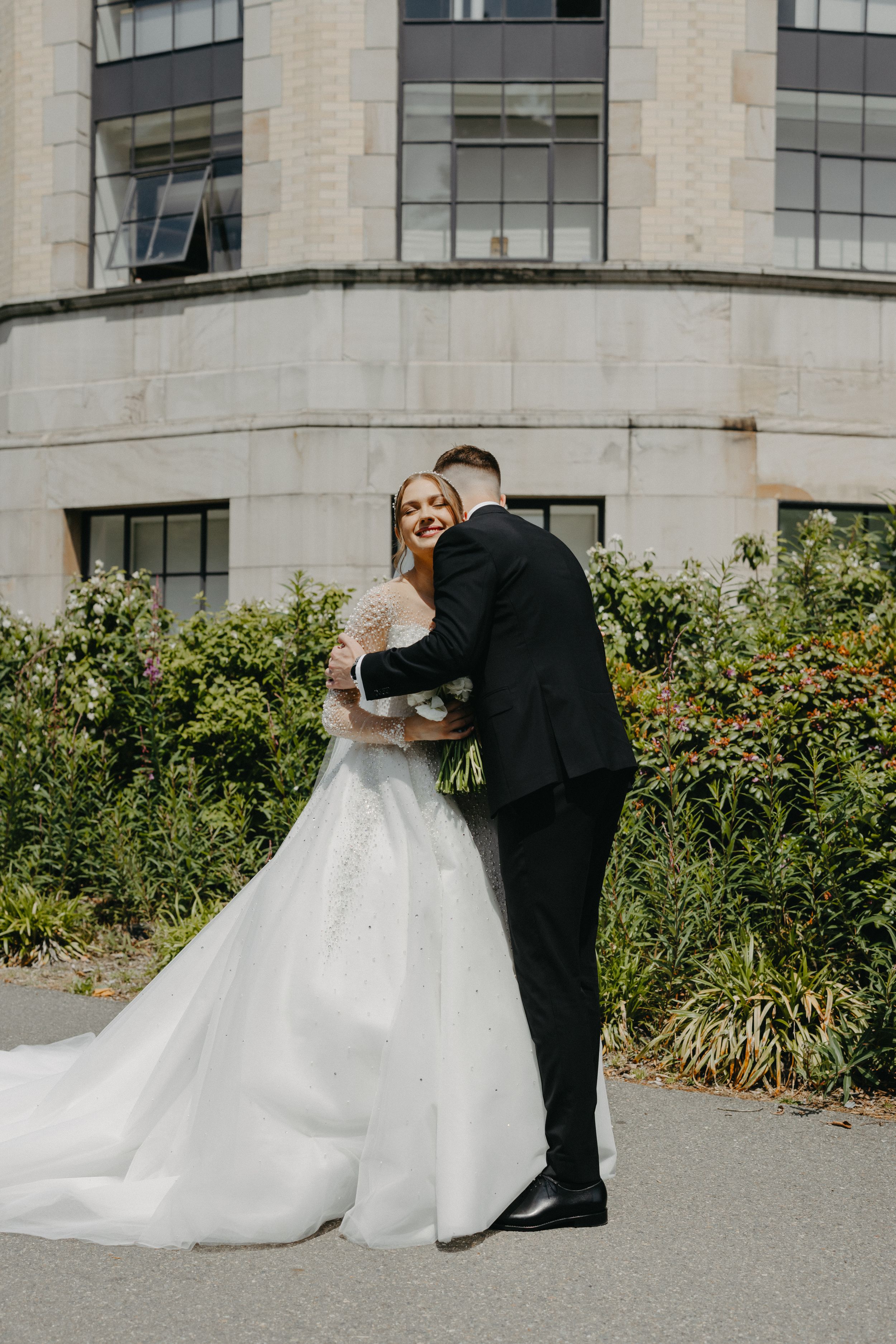 Newlyweds sharing an intimate moment outside a stone building with garden landscaping.