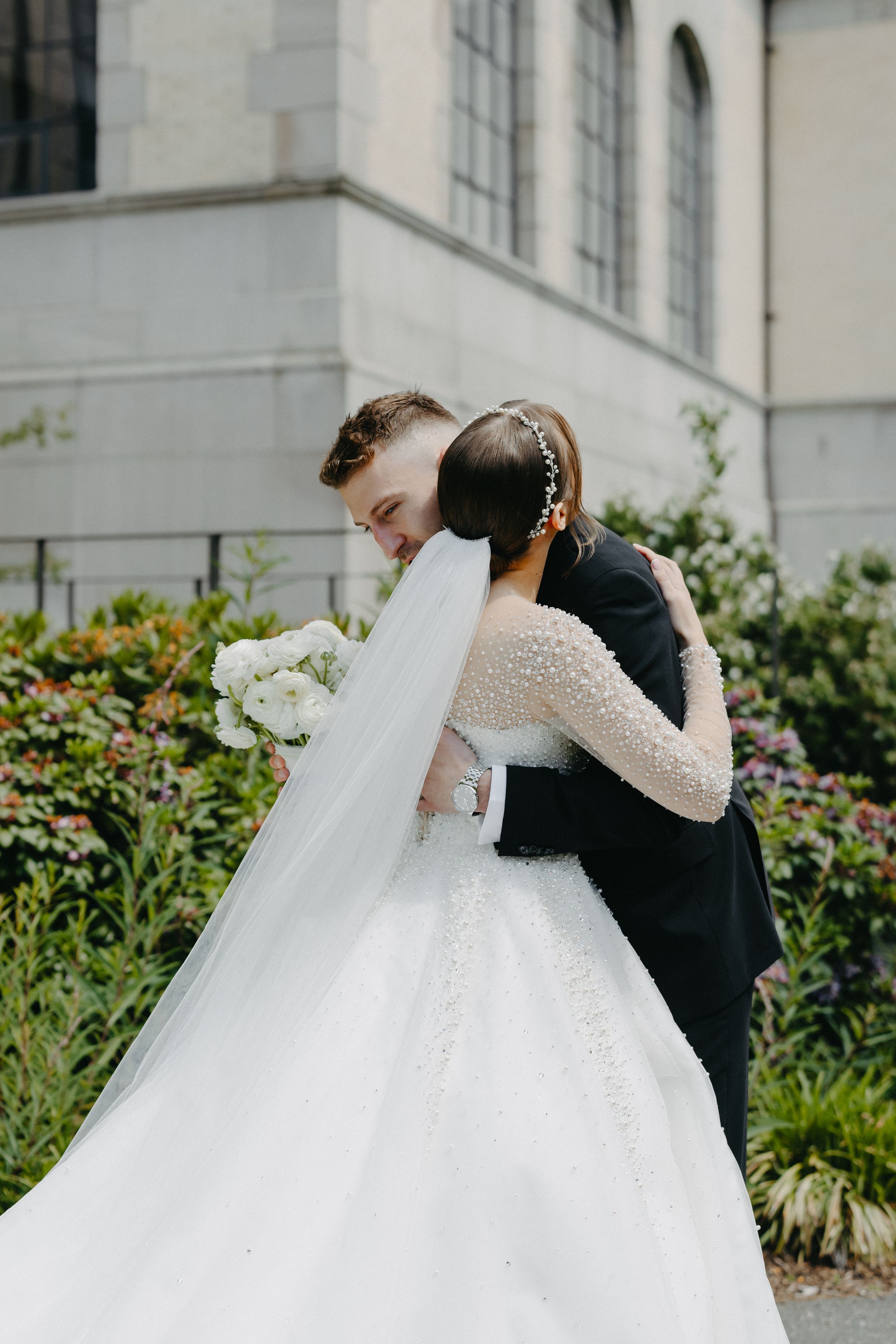 A romantic embrace between newlyweds outside a church with white flowers.