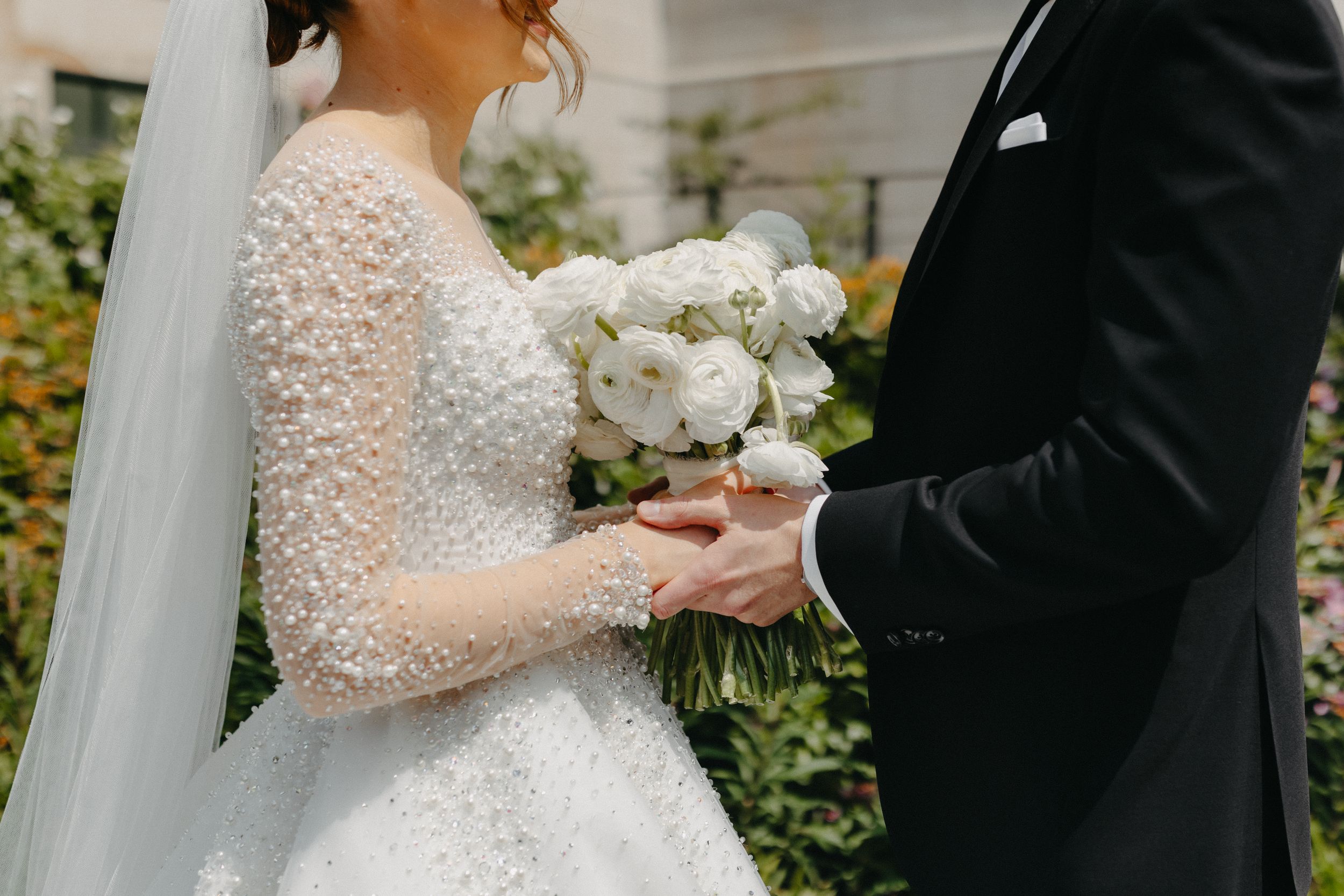 A close-up shot of a wedding couple's hands holding a white rose bouquet.