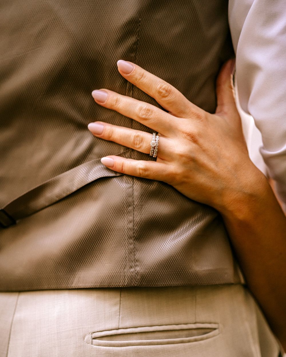 brides ring hand reaches around grooms back