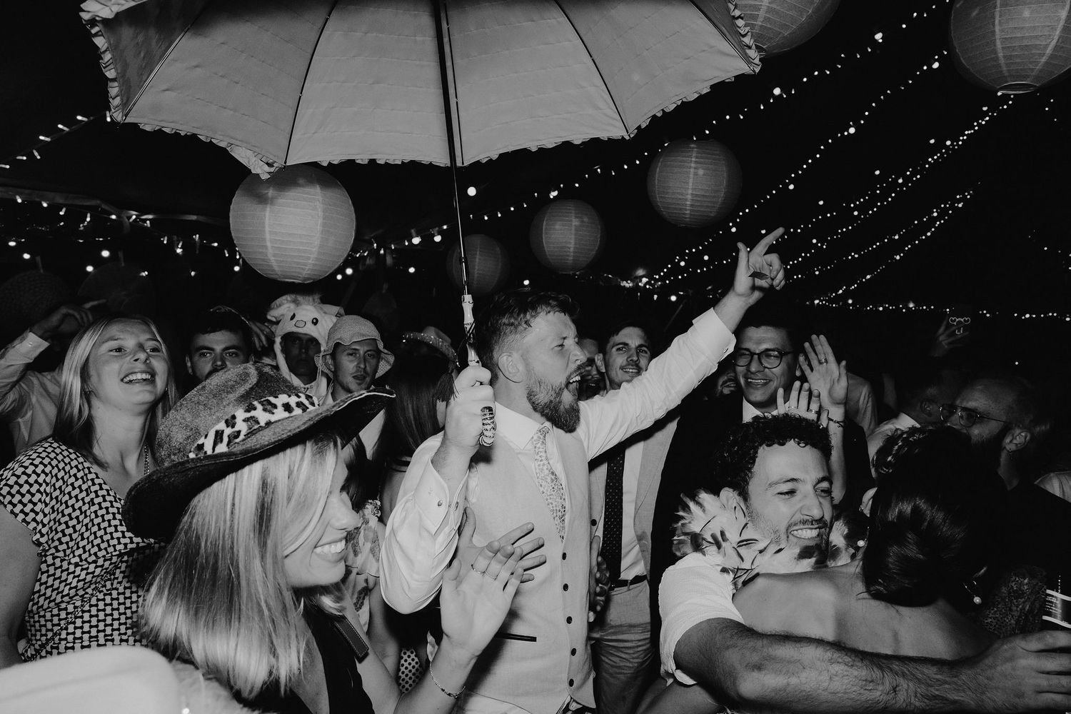 groom standing underneath an umbrella he's holding on a busy dance floor at wedding in oxfordshire