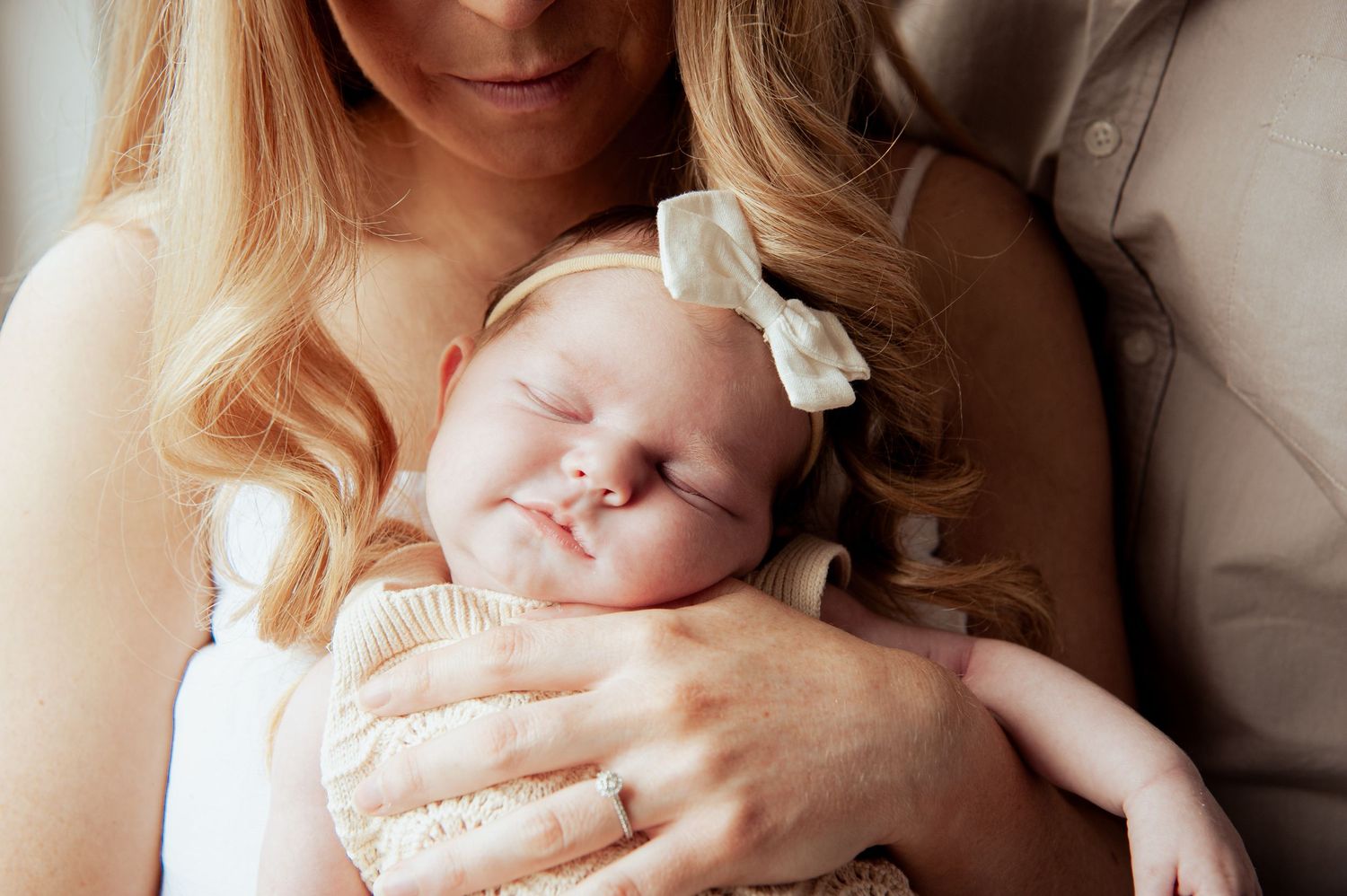 Peaceful sleeping newborn baby wearing white bow headband nestled in parent's arms.
Altona Family Photographer Melbourne