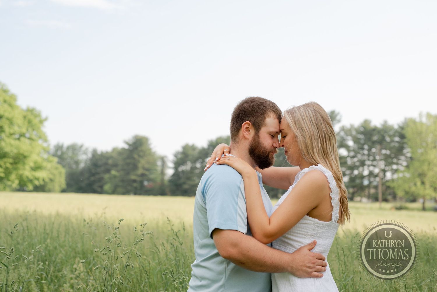 An intimate outdoor portrait of a couple sharing a close moment in a grassy field.