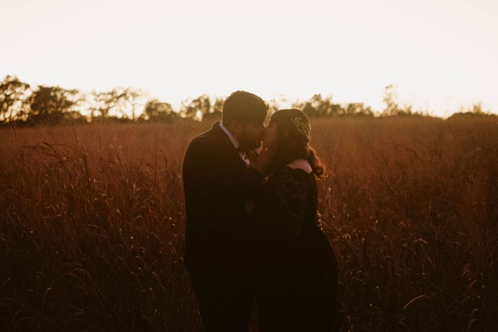 Silhouetted pair sharing tender moment in field at dusk.