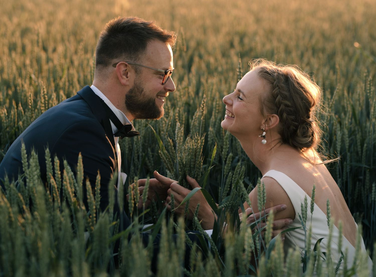 Couple sharing a joyful moment in a golden wheat field at sunset.