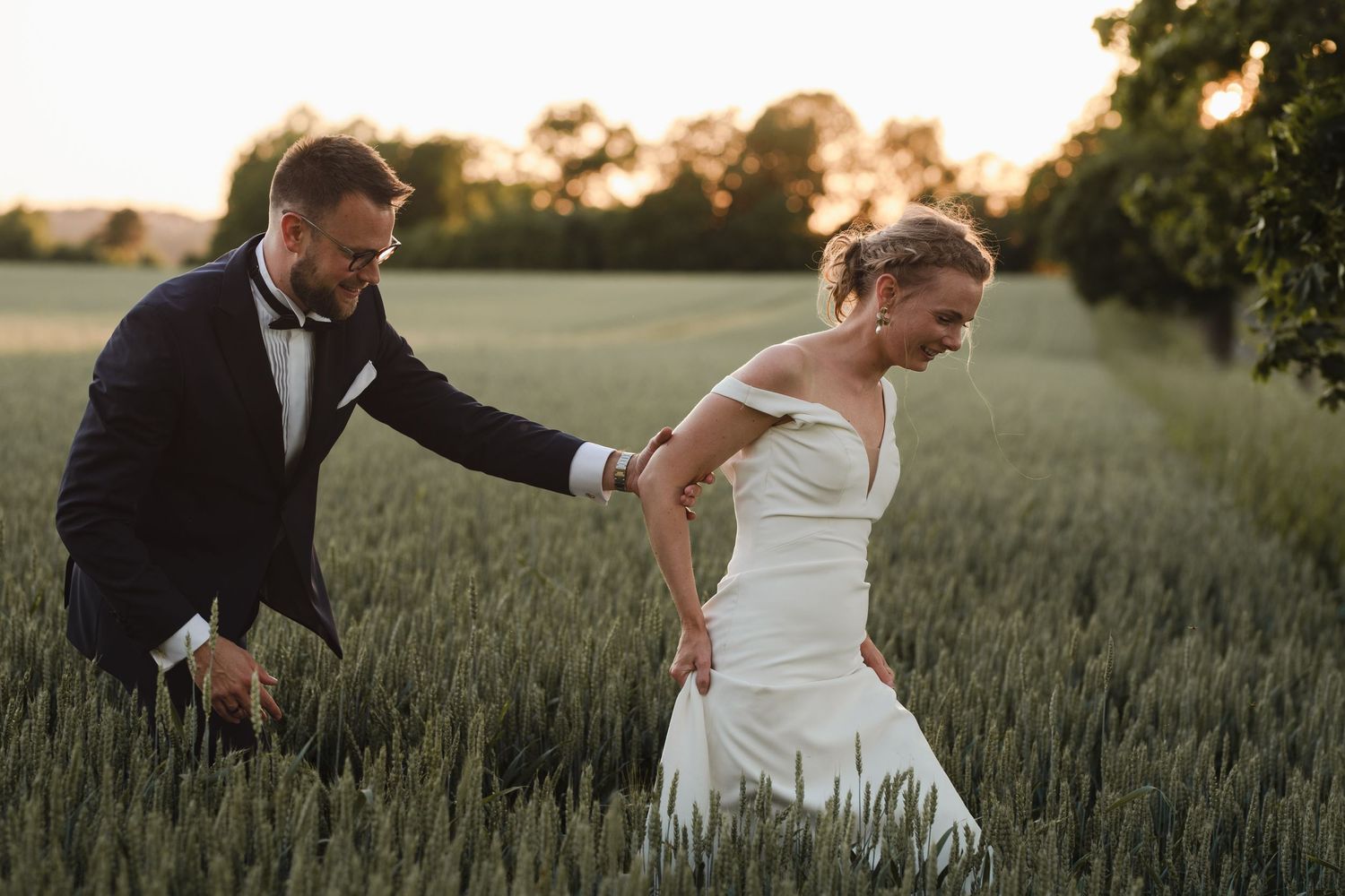 Playful moment between newlyweds in a wheat field during sunset.