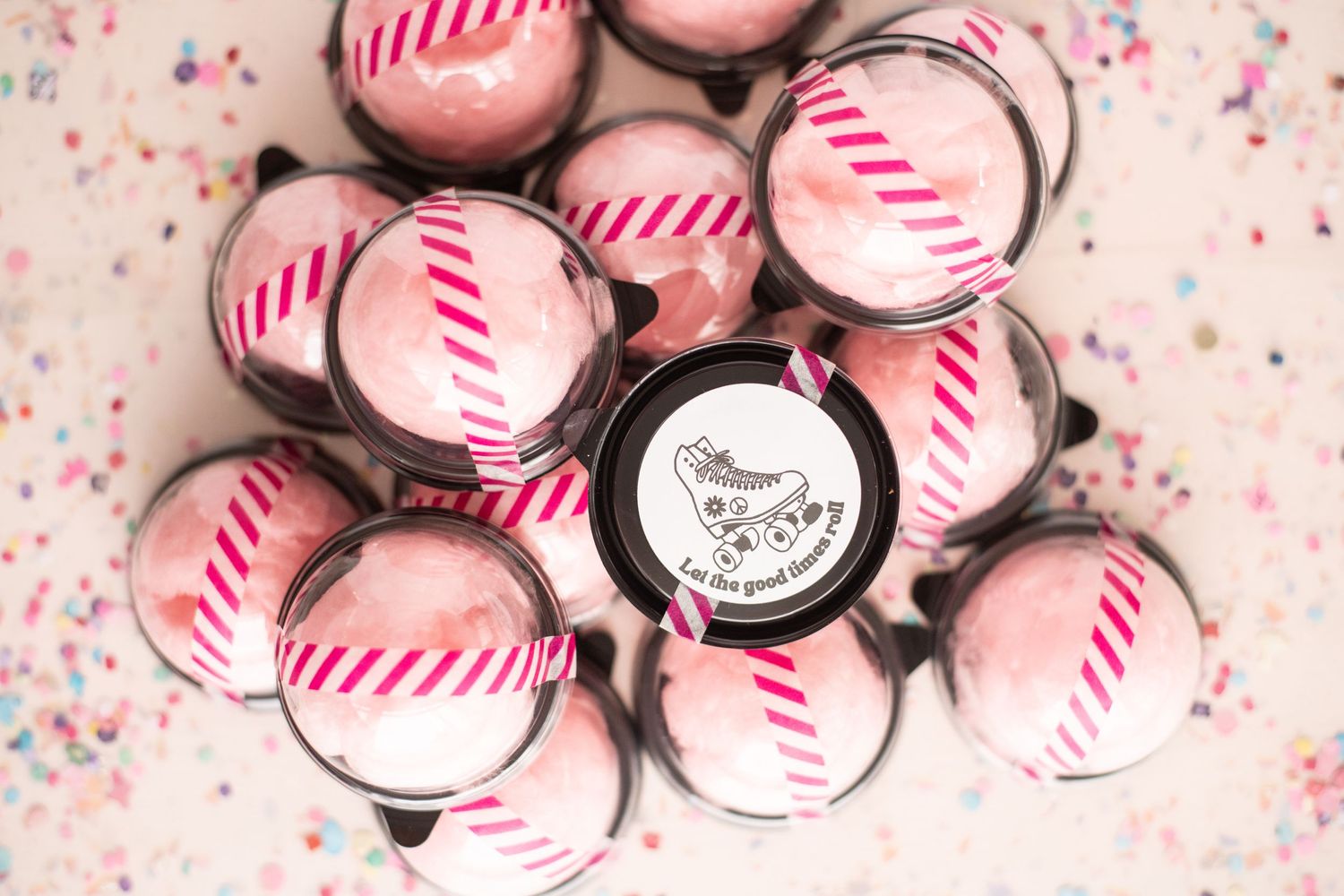 Pink and white striped bottle caps arranged with confetti on pink background.