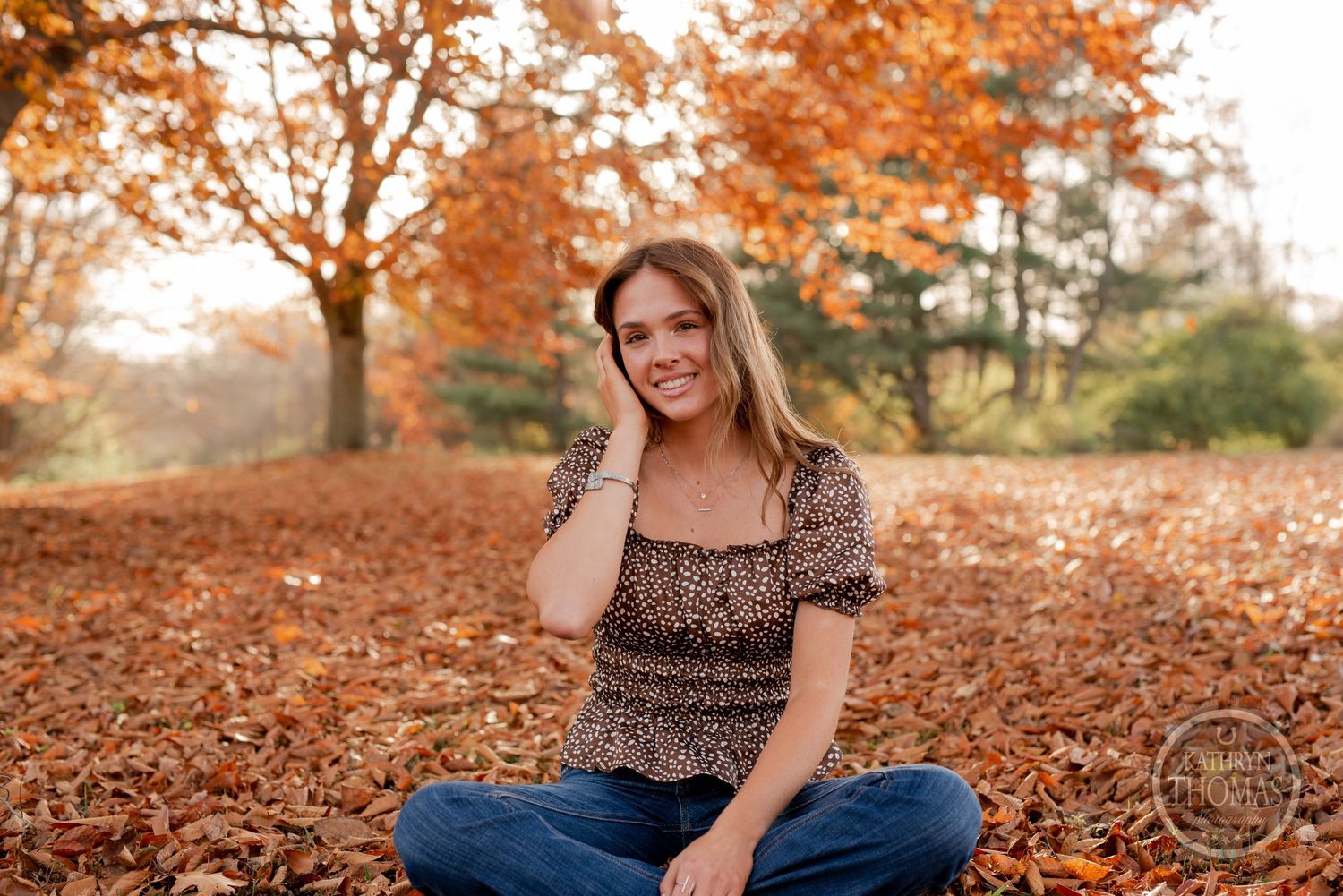 An outdoor portrait sitting among fallen autumn leaves with orange trees in the background.