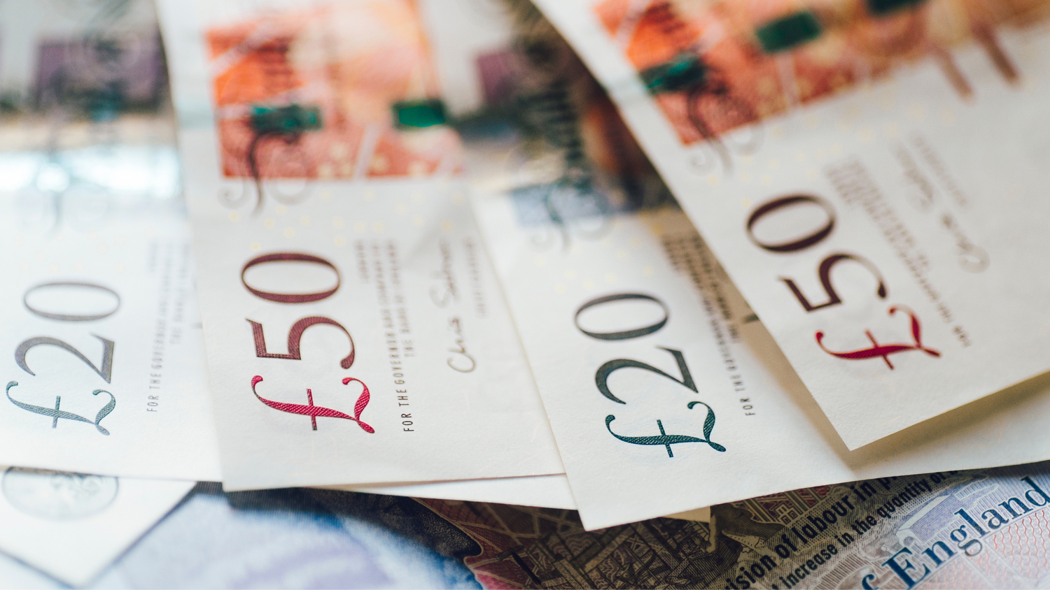 Close-up of British pound notes showing various denominations in soft focus.