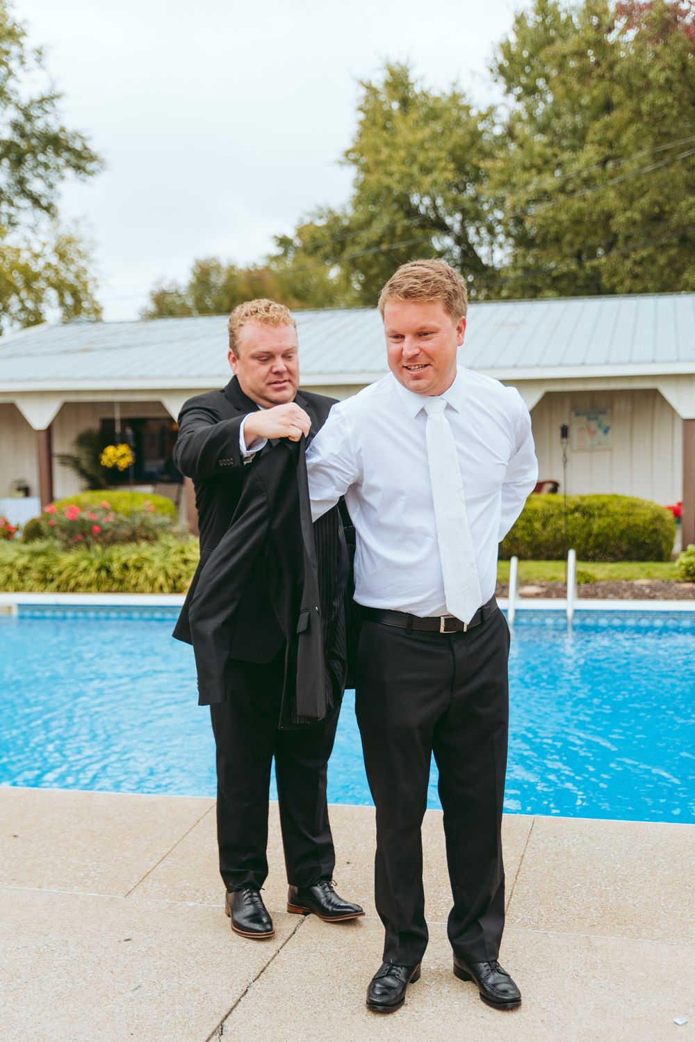 Groom's brother helps him put on his black jacket.