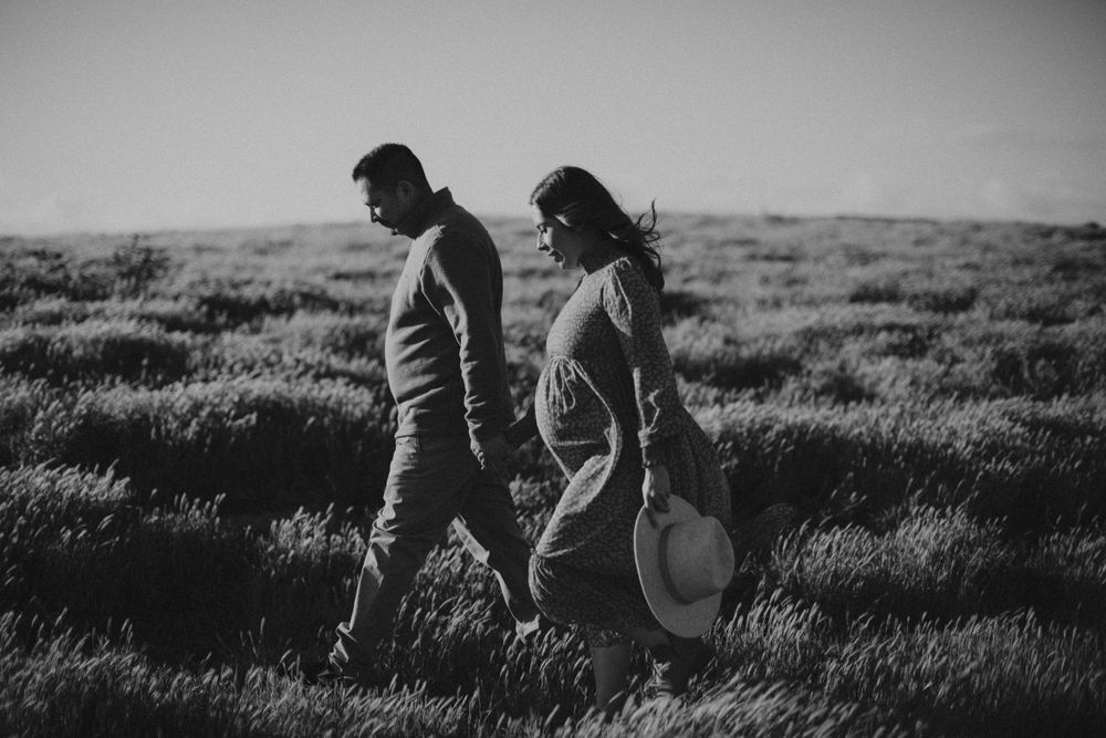 A couple walks through tall grass in a black and white landscape photo.