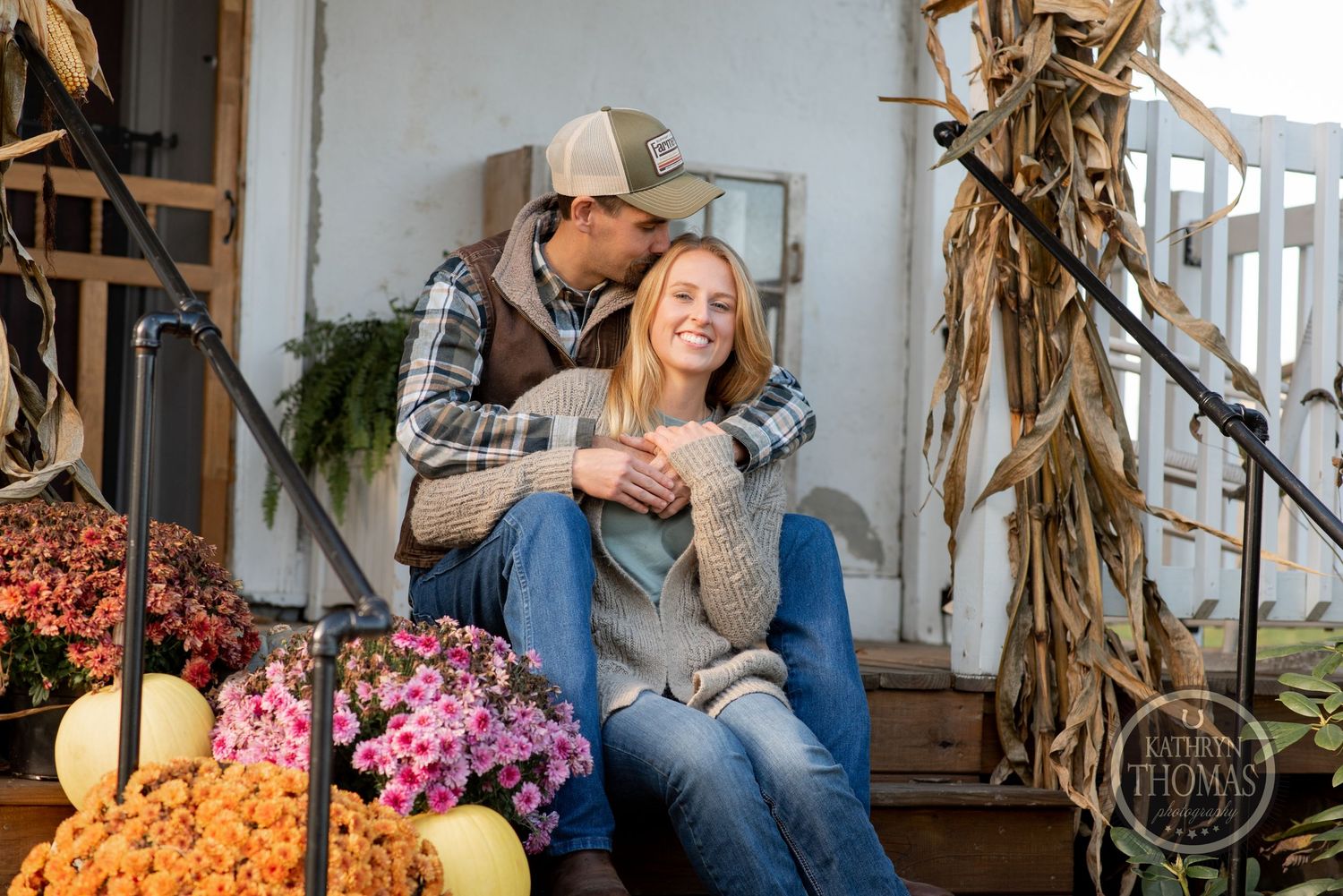Couple relaxing on porch steps decorated with fall flowers and pumpkins.