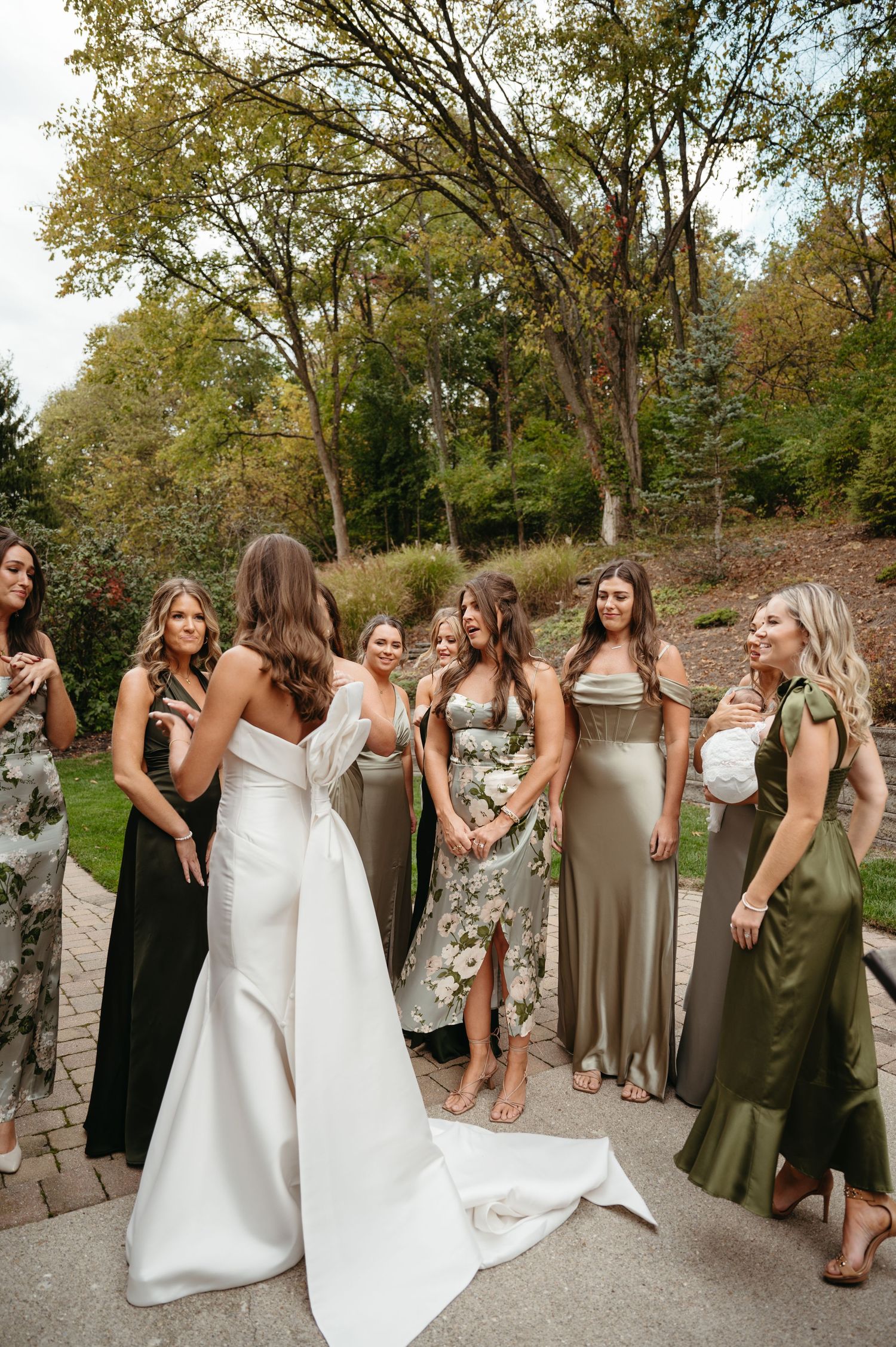 A bridal party in mixed-length dresses gathers outdoors during an autumn wedding celebration.